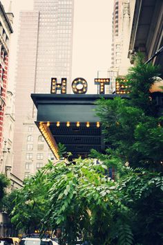 the hotel sign is lit up in front of some tall buildings and greenery outside