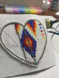 a piece of beaded art with a heart on it and scissors next to it