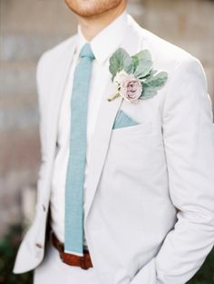 a man in a white suit with a blue tie and flower on his lapel