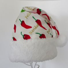 "\"Feliz Navidad\" is the message on this south of the border celebration Santa hat. This festive Santa style hat is made up in an ivory cotton fabric with gold lettering bold red and green chili peppers in the print . The slouch cone style hat is accented with snowy white soft faux fur fabric trim and there is a fluffy white pompom stitched on the top. Proportions of the hat are generous and will fit most head sizes, ladies or gents. Measurement for opening for your head is 26\" circumference a Christmas Party Hat, Las Vegas Christmas, Christmas Party Hats, Adult Christmas Party, Green Chili Peppers, Bad Santa, Santa Costume, Santa Claus Hat, Earring Storage