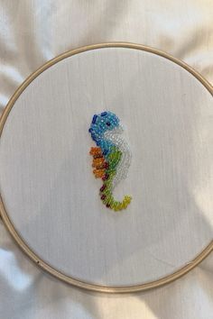 a cross stitch seahorse is displayed on a white fabric covered surface in a gold hoop