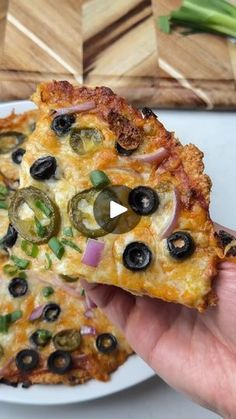 someone holding up a slice of pizza with olives and onions on it