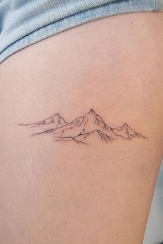 a woman's thigh with a small mountain tattoo on the back of her leg