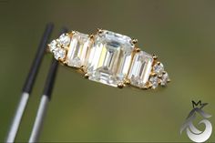 an emerald cut diamond ring on top of a pair of tongs with two diamonds in the middle