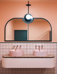 two pink sinks under a mirror in a bathroom with tiled walls and flooring below them