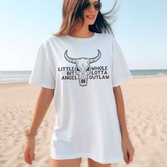 a woman standing on the beach wearing a white shirt with an image of a bull's head