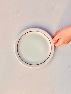 a white plate with red trim is being held by someone's hand over the edge