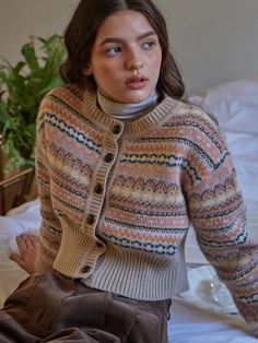 a woman sitting on top of a bed wearing a sweater and pants with an open collar