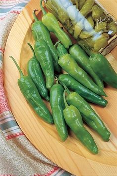 green peppers on a wooden plate next to a jar of pickles