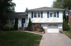 a white house with blue shutters on the front door and brick walkway leading up to it