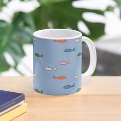 a blue coffee mug with fish on it sitting on a table next to a book