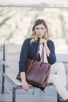 a woman sitting on a bench holding a brown purse