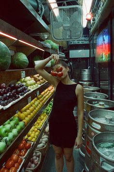 a woman in a black dress standing next to a shelf filled with fruits and vegetables