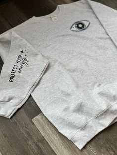 About this product - This Crewneck boasts an oversized Evil Eye Design and Arm Sleeve Accent -Pocket Design is Approx. 5in x 3in -Sleeve Design is Approx. 7in x 2in - Unisex Sizing  - Crewneck is either Gildan Softstyle or Hanes EcoSmart  - Screen Printed or DTF (Direct to Film)  - Wash inside out - No Fabric Softener  - Tumbler Dry Low or Hang Dry - Shirts are Made to Order  -Please allow 7-10 business days for shipping notifications. Trendy Relaxed Fit Sweatshirt With Pockets, Trendy Gray Sweatshirt With Pockets, Oversized Long Sleeve T-shirt With Pockets, Trendy Crew Neck Sweatshirt With Pockets, Oversized Sweatshirt With Side Pockets, Oversized Sweatshirt With Side Pockets For Everyday, Gray Long Sleeve Sweatshirt With Side Pockets, Trendy Oversized Short Sleeve Sweatshirt, Everyday Long Sleeve T-shirt With Pockets