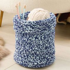 a blue and white basket with yarn, knitting needles and crochet hooks in it