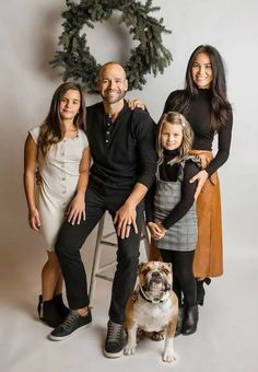 a family posing for a photo with their dog and christmas wreath in the back ground