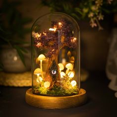 a glass dome with some lights in it on a table next to plants and flowers