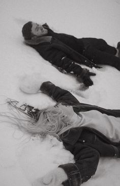 two people laying in the snow on their stomachs, one with her hair blowing back