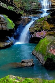 a small waterfall in the middle of a forest with moss growing on it's sides