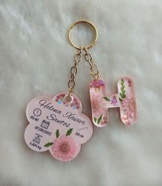 two key chains with flowers on them sitting on a white surface, one has a name tag and the other has a flower