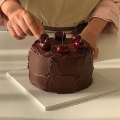 a person cutting into a chocolate cake with cherries on it