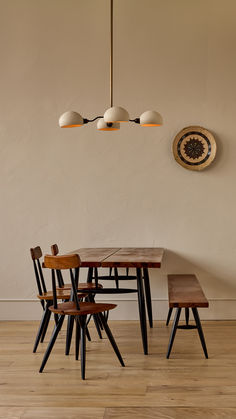 a wooden table and four chairs in front of a wall with two hanging lights above it