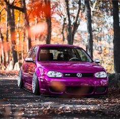 a purple car parked on the side of a road in front of trees and leaves