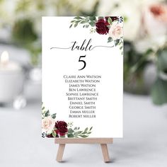 a table number card with flowers and greenery on it, sitting on top of a wooden easer