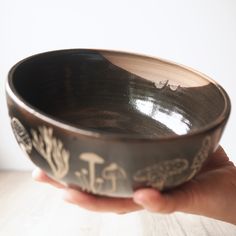 a hand holding a black and brown bowl on top of a wooden table