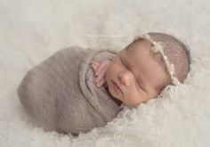 a newborn baby wrapped in a blanket is laying on a white surface and smiling at the camera