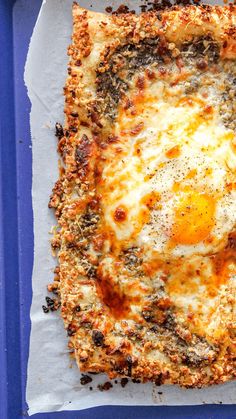 a square pizza with an egg in it on top of white paper and blue tray