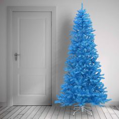 a bright blue christmas tree stands in front of a white door and wooden flooring