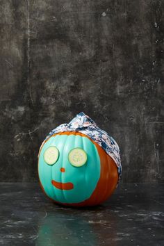 an orange and blue pumpkin with cucumbers on it's face sitting on a table