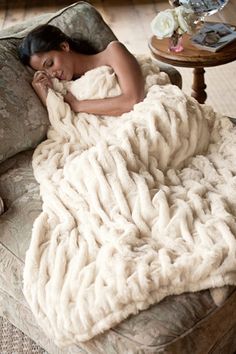 a woman laying on a couch covered in a blanket