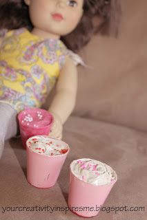 a small doll sitting on top of a couch next to two cups with something in them