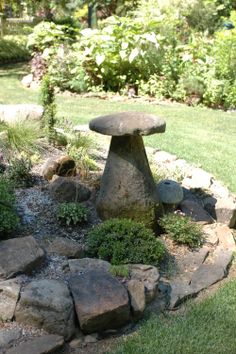 a stone bench sitting in the middle of a lush green field next to some rocks