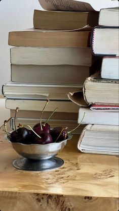 a bowl filled with cherries sitting on top of a wooden table next to books