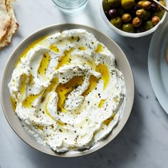 a bowl of hummus with olives and bread on the side