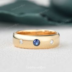 a yellow gold band with three diamonds and a blue sapphire in the center, sitting on a white surface