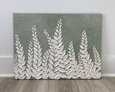 a painting with white leaves on it sitting on top of a hard wood floor next to a wall