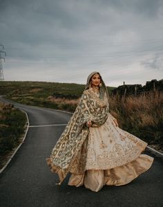 a woman is standing on the road wearing a long dress and veil with her hands in her pockets