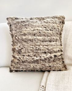 a close up of a pillow on a couch with a white throw blanket behind it