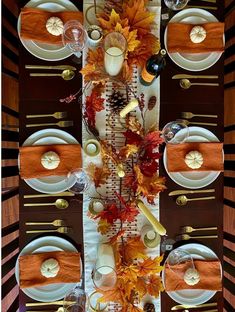 the table is set with white plates, silverware and autumn leaves on it's placemats