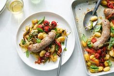 two white plates with sausages and pasta on them next to glasses of wine, silverware and utensils