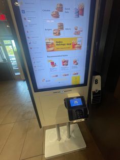 a digital menu kiosk machine in front of a large screen with food items on it