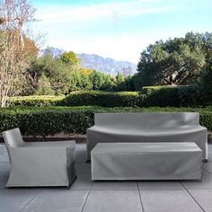 a couch and chair sitting on top of a cement floor next to bushes with mountains in the background