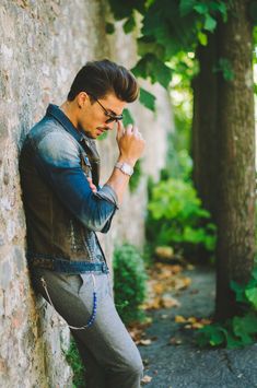 a man leaning against a stone wall with his hand on his chin and looking down