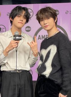 two young men standing next to each other in front of a purple wall and microphone