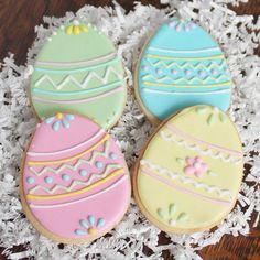 three decorated cookies sitting on top of white shredded paper next to an egg shaped cookie