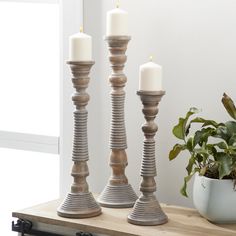 three candles sitting on top of a wooden table next to a potted plant and window